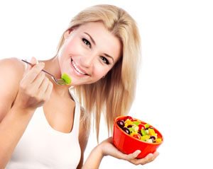 Pretty girl eating fruit salad in a bowl with spoon